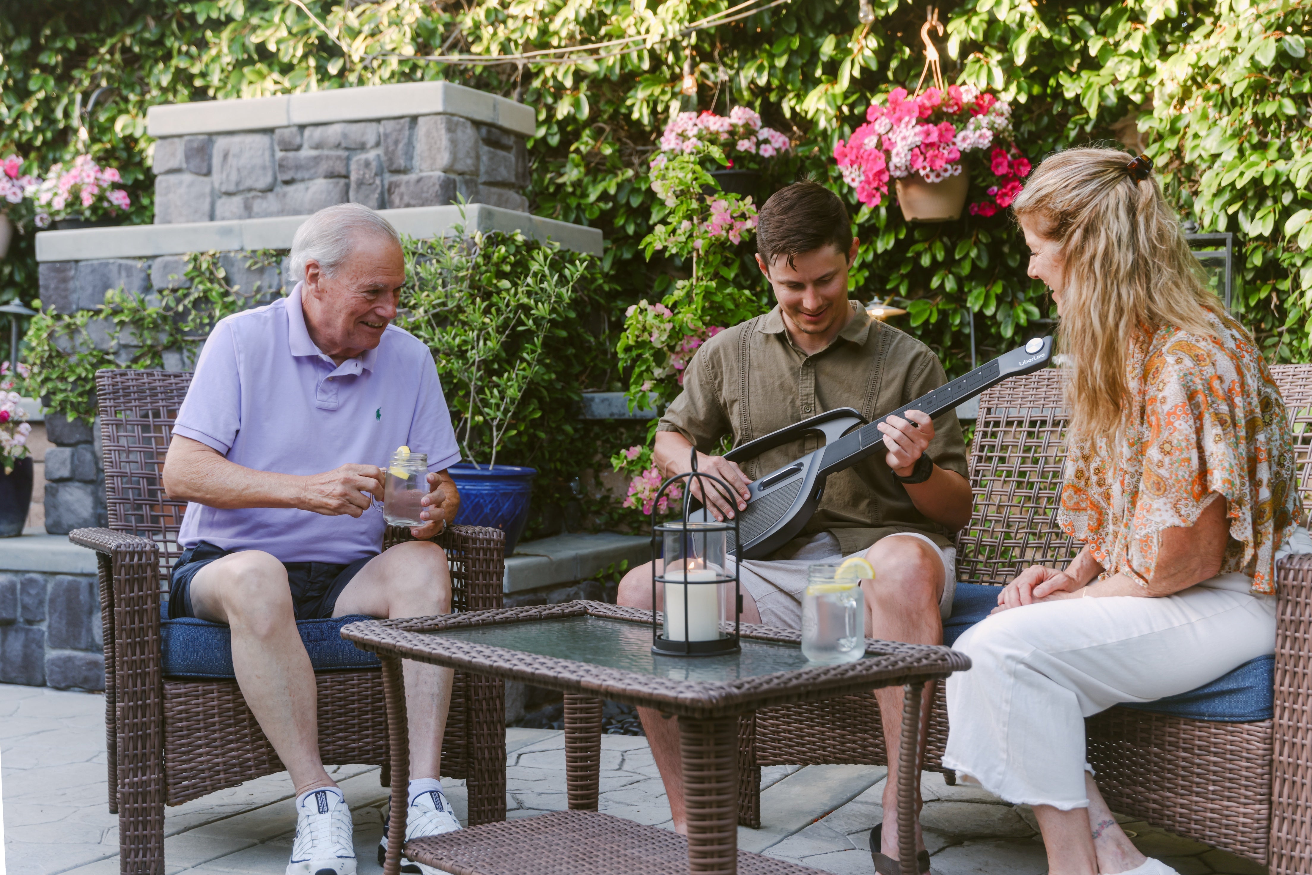 Friends listening to a black LiberLive C1 smart guitar on a backyard patio
