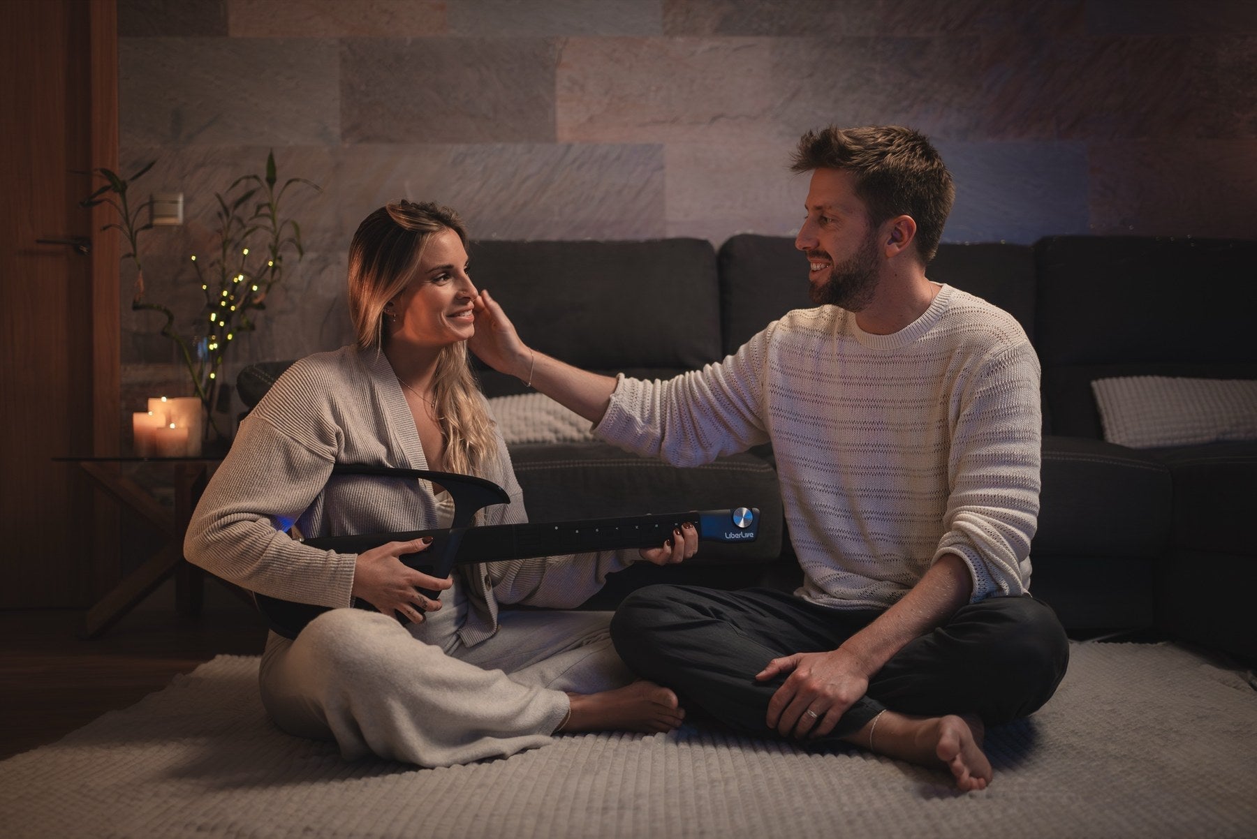 Two people reviewing a black LiberLive C1 smart guitar in a home setting