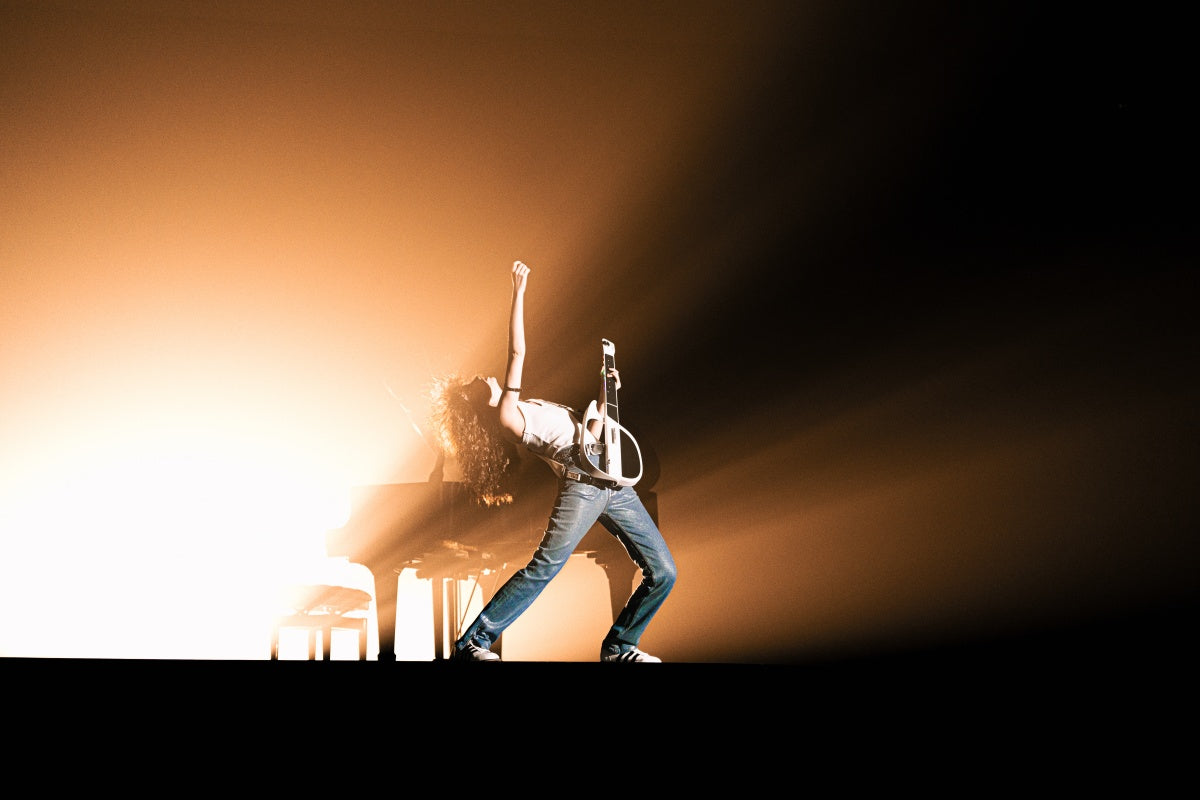 Performer playing a LiberLive C1 smart guitar on stage under warm spotlights.