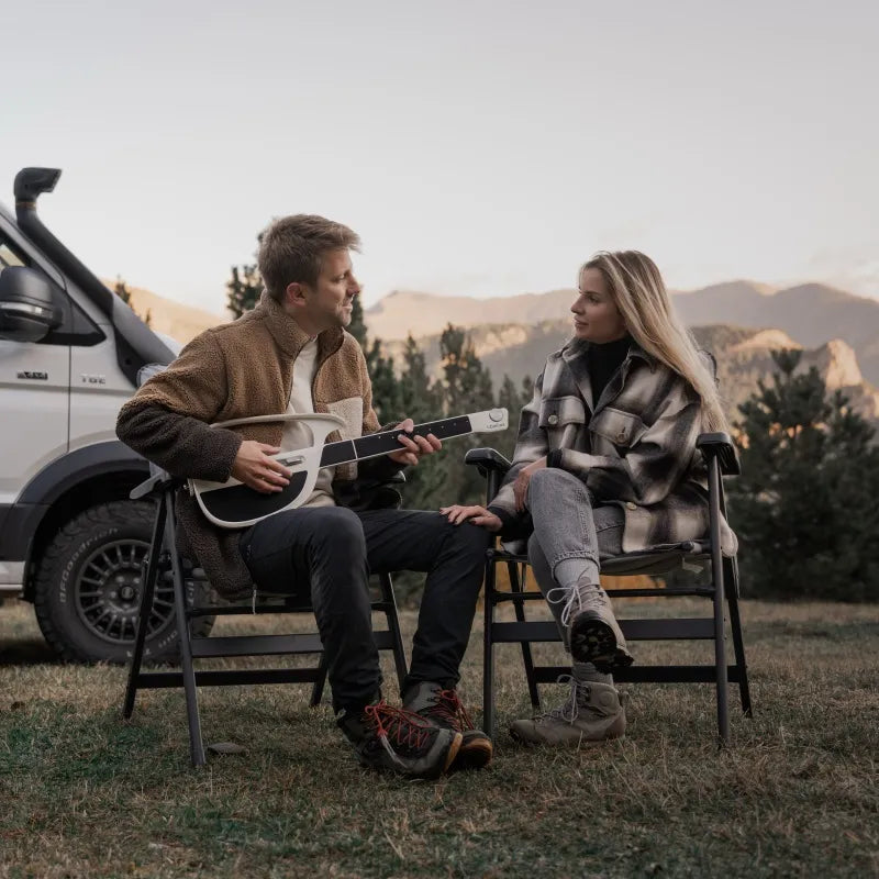 Outdoor couple sitting by a vehicle while one person plays a white LiberLive C1 travel smart guitar.